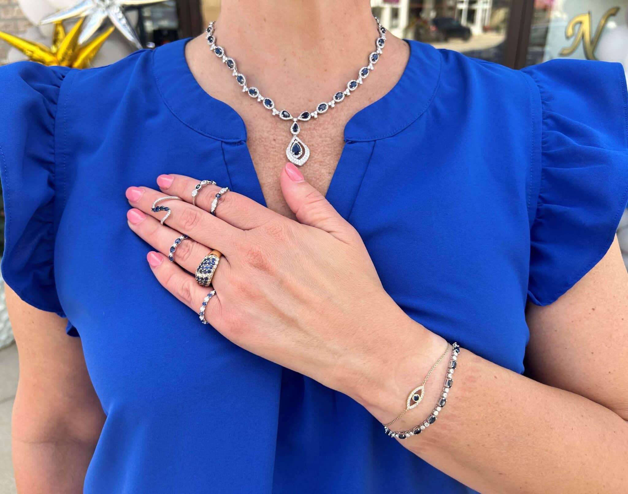 Woman wearing a sapphire necklace, two sapphire bracelets, and six sapphire rings.